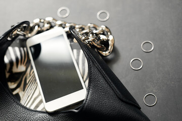 Black leather bag with chain, white phone, zebra print, silver thin rings on a black background © Oksana Smyshliaeva