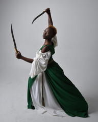 Full length portrait of pretty African woman wearing long green medieval fantasy gown holding ...