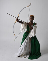 Full length portrait of pretty African woman wearing long green medieval fantasy gown holding bow...