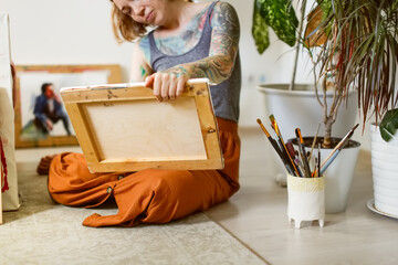 Charming caucasian red-haired woman artist with tattoos in home studio, light photography of...