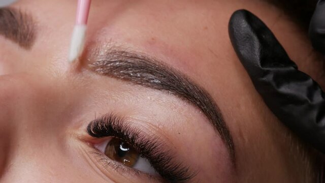 Applying a special fixing gel with a cotton swab. A beautiful young girl model with ready made permanent makeup for eyebrows. Microblading, permanent makeup tattoo close up view