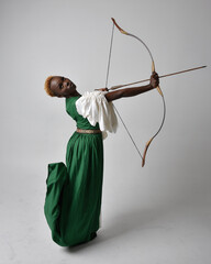 Full length portrait of pretty African woman wearing long green medieval fantasy gown holding bow...