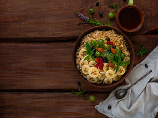 Wholegrain Oatmeal porridge bowl with fresh berries, fruits, nuts mint leaves tea cup. Healthy food oat meal morning breakfast top view. Whole grain cereal gooseberry currant banana on wooden table.