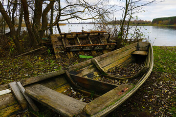 Fototapeta na wymiar An old wooden wrecked boat on the shore of the lake in the fall.
