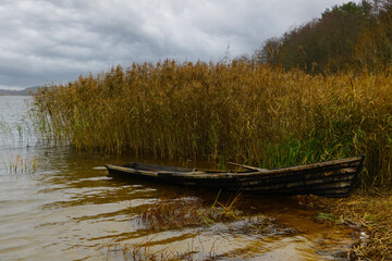 Obraz premium An old boat on the shore of the lake in the autumn on a cloudy day.