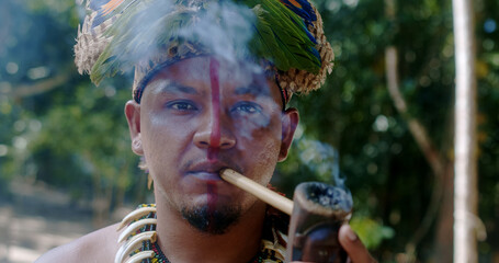 Indian chief from the Pataxó tribe smoking pipe . Brazilian Indian with feather headdress and...