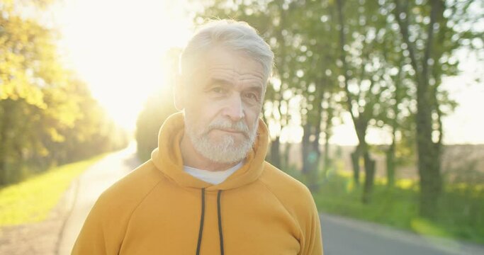 Close up portrait of joyful positive Caucasian handsome old man in good mood smiling at camera standing on street in sun lights in the morning. Happy senior male with smile on face, outdoor concept