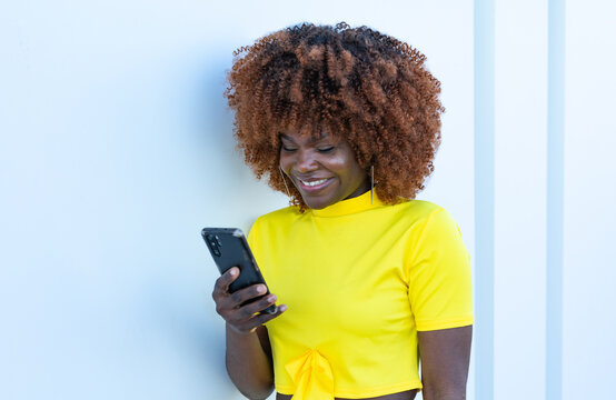 Chica sonriente africana mirando el teléfono móvil.