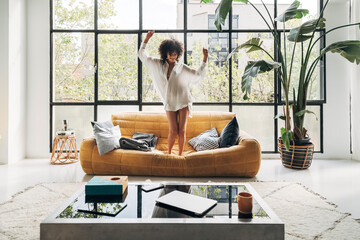 Young multiracial woman dancing to music on the couch in a bright living room