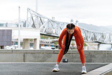 Young athlete stop to rest while running. Copy space. Tired woman bending over to catch her breath...