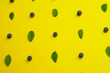 Blueberries with leaves laid out as a pattern on a bright yellow background in flat lay style, top view
