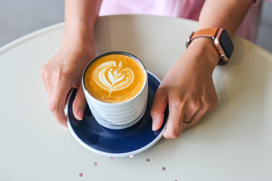 Closeup image of a woman holding a white cup of coffee with latte art