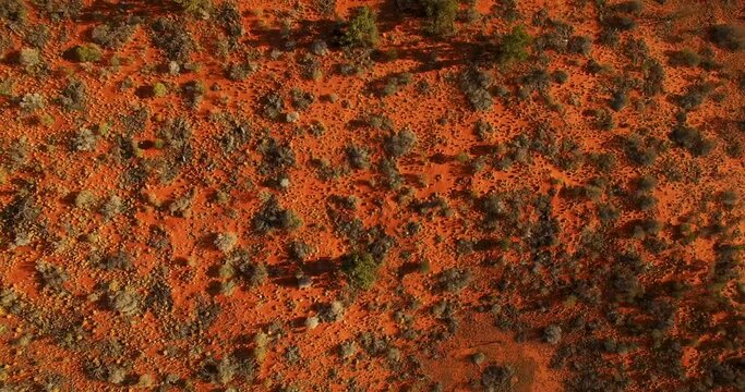 Slow moving aerial across a red earth Australian landscape, to tilt up and reveal a vast outback landscape