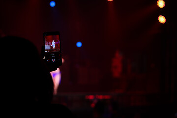 Fototapeta na wymiar Audience taking photo and recording video of sexy woman dancing on stage, girl showing on stage concert with colorful glow bright spotlights on dark background.