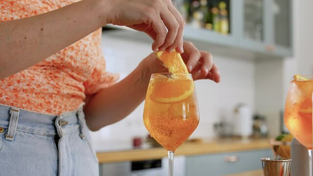 drinks and people concept - happy smiling young woman making orange cocktail at home kitchen