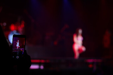 Audience taking photo and recording video of sexy woman dancing on stage, girl showing on stage concert with colorful glow bright spotlights on dark background.