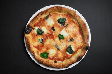 top view of margarita pizza with tomatoes, cheese and basil on black background