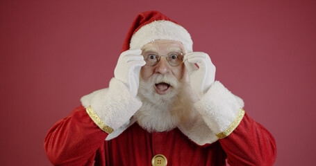 Santa Claus in eyeglasses is looking at camera and smiling, on red background
