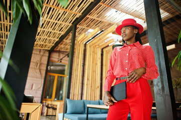 Pretty braids business african american lady bright bossy person friendly wear office red shirt, hat and trousers, hold tablet on hands.