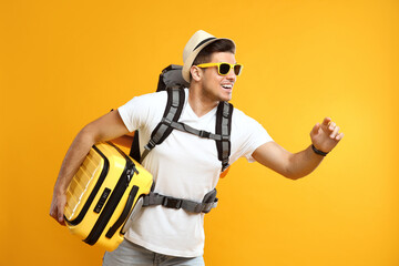 Male tourist with travel backpack and suitcase on yellow background