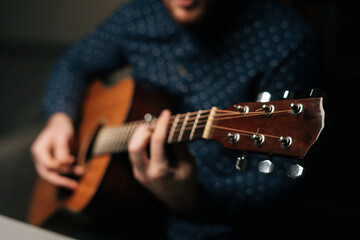 Close-up of unrecognizable guitarist singer male playing acoustic guitar sitting on armchair in...