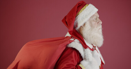 Real Santa Claus with a red background, wearing glasses, gloves and a hat looking side.