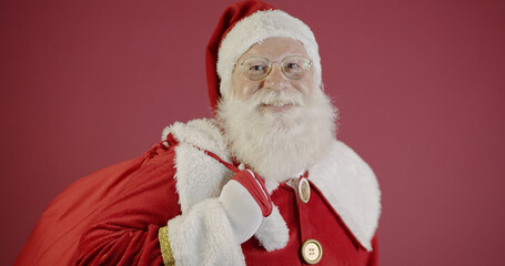 Real Santa Claus with a red background, wearing glasses, gloves and a hat looking side.