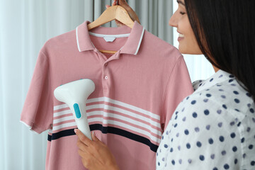 Woman steaming shirt on hanger at home, closeup
