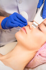 Naklejka premium Closeup of beautiful young woman receiving ultrasound facial exfoliation and cavitation facial peeling with ultrasonic equipment in cosmetology office