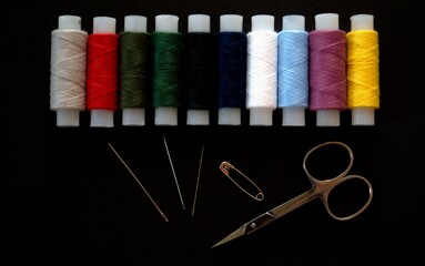 Multicolored reels with sewing threads on a black background. Scissors, needles and pins