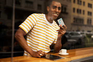 Handsome young african man in cafe drinking coffee. Portrait of happy man with credit card drinking coffee in cafe.