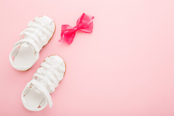 White sandals and ribbon for little girl on light pink table background. Pastel color. Closeup....