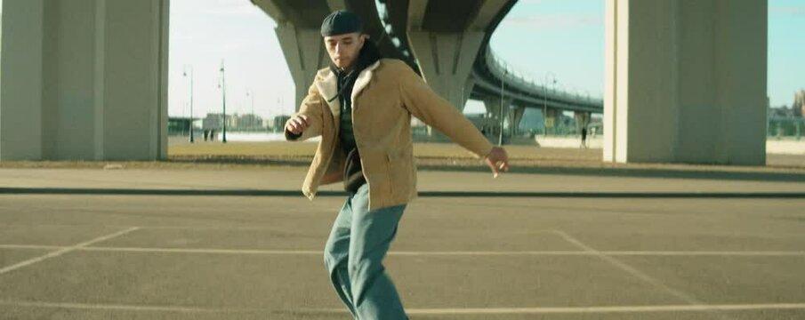 Anamorphic shot of young man in streetwear dancing hip hop under urban bridge