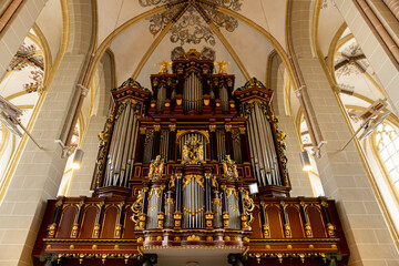 High church body arches with richly decorated organ with golden ornaments on the metal pipe structure. Religious music instrument in cathedral.