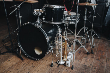 A black and gray drum kit with cymbals and a microphone stand are on stage and next to them are two trumpets (alto and bass) and a white tambourine. The concept of a live concert of a jazz band.