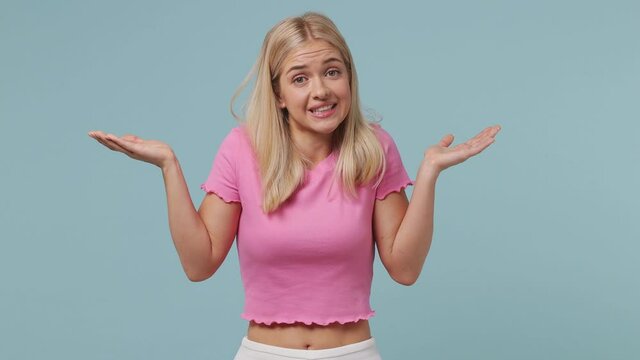 Fun confused shy shamed young blonde woman 20s wears pink t-shirt look camera spreading hands say oops ouch oh omg i am so sorry isolated on pastel plain light blue color background studio portrait