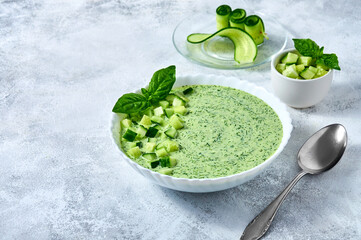Cucumber Gazpacho - cold summer soup with basil in white bowl on light background