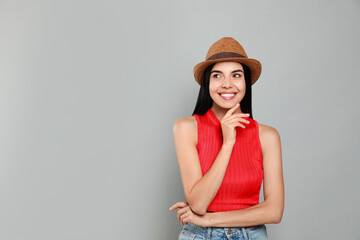 Beautiful young woman with straw hat on light grey background. Space for text