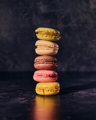 A tower stack of five colourful macaroons on a dark textured background, isolated.
