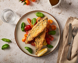 Lightly battered and fried mackerel fish and tomato basil salad on table setting, light and airy summer dinner or lunch