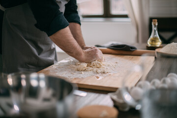 A male chef prepares noodle dough at home in the kitchen. Close up of hands with flour and dough