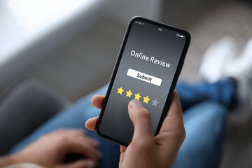 Man using smartphone to give feedback indoors, closeup. Customer review