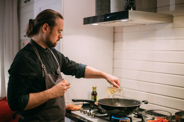 A male cook is cooking at the stove at home in the kitchen