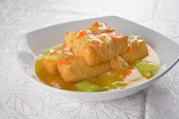 Deep fried bean curd tofu with luffa melon in yellow chicken stock sauce and crab meat on white background Asia halal menu