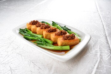 Deep fried bean curd tofu with minced meat on top and vegetables in dark soy sauce on white background Asia appetiser halal menu