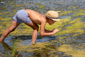 a boy in a hat is catching frogs in a swamp