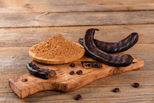 Dry carob pods and carob powder over wooden background. Organic healthy ingredient for vegan vegetarian food and drinks, close up