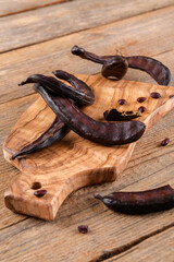 Dry carob pods on wooden background. Organic healthy ingredient for vegan vegetarian food and drinks, close up