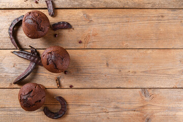 Chocolate carob cupcakes cooking with carob powder and dried carob pods on a wooden background. Organic healthy sweet food for vegan vegetarian food and drinks, copy space