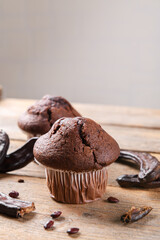 Chocolate carob cupcakes cooking with carob powder and dried carob pods on a wooden background. Organic healthy sweet food for vegan vegetarian food and drinks, close up